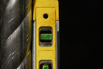 Construction spirit level aligned vertically next to metal surface on black background.