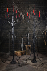 Forged wrought iron floor candelabras with twisted columns and lit red candles in dark medieval castle stronghold interior.