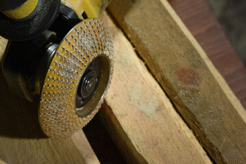 Electric angle grinder with carbide rasp disc placed on light stone blocks on workshop surface with dark close up background.