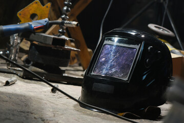 Protective welding mask visor with adjustment knobs showing worn transparent screen on industrial workshop background.