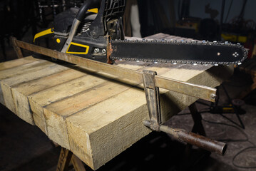 Chainsaw fixed with metal clamp on wooden beam during woodworking process in dark workshop environment background close up.