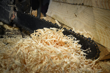 Chainsaw cutting wooden beam with fresh sawdust pile in workshop environment close up background.