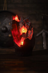 Carved wooden candle holder made from burned tree log with embedded glowing electric candles bulb emitting warm red light in dark atmospheric interior.