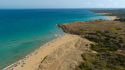 Aerial view of Pizzuta beach located in the Vendicari nature reserve in the province of Syracuse, Sicily, Italy. The sea stretches to the horizon with colours ranging from turquoise to blue.