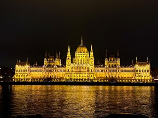 Fototapeta premium Parliament glowing brightly at night in Budapest, Hungary. View across the Danube River.