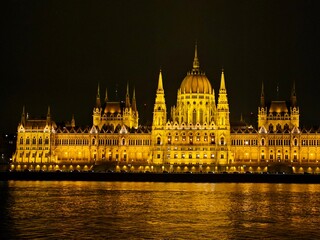 Fototapeta premium Parliament glowing brightly at night in Budapest, Hungary. View across the Danube River.