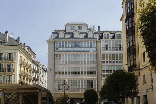 View of bright sunlight illuminating the elegant facades of buildings with white window frames, creating a striking contrast against the clear sky, Santander, Cantabria, Spain.