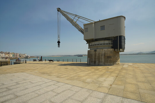 View of Gr&uacute;a de Piedra crane stands prominently on a paved platform overlooking the tranquil blue bay waters, a historic industrial relic, Santander, Cantabria, Spain.