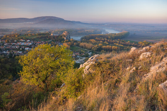 View of golden sunlight bathes the rugged terrain, the castle ruins amidst a tranquil river winding through the landscape, Devinska Nov&aacute; Ves, Bratislava Region, Slovakia.