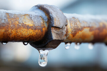 Close up of frozen rusty metal pipe with ice droplets and frost in severe winter weather conditions.