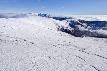 View of the serene white snow blankets the rugged mountain peaks under a clear blue sky, contrasting with the distant cloudy horizon, Nizke Tatry, Banska Bystrica region, Slovakia.