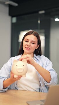 Young woman happily saves money, placing coin into piggy bank. Financial planning for secure future. Indicates happiness, confidence, and smart investment.