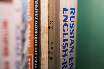 Macro shot of old Russian-English dictionary spines on a bookshelf. Selective focus emphasizes the concept of education, translation, and learning a new language. Vintage, academic feel.