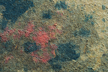 Abstract texture of weathered wood with patches of red and blue paint on a natural fiber background