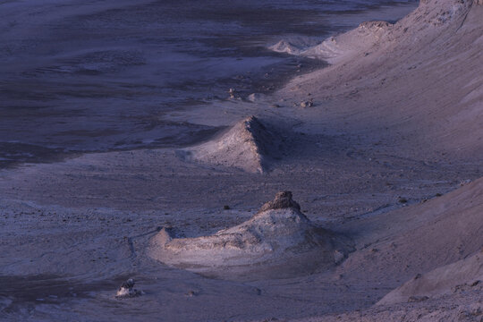 View of stark, moonlike terrain, etched with shadows and sculpted by wind, reveals a desolate beauty under a twilight sky, Karynzharyk, Mangystau Region, Kazakhstan.