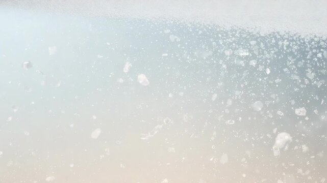 Drifting pale specks and clumps from subtle motion across macro pastel gradient, forming right pile