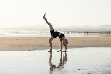 Woman practicing yoga wheel pose on beach at sunset