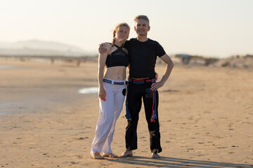 Capoeira practitioners standing on beach embracing at sunset