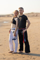 Capoeira practitioners standing on beach displaying belts
