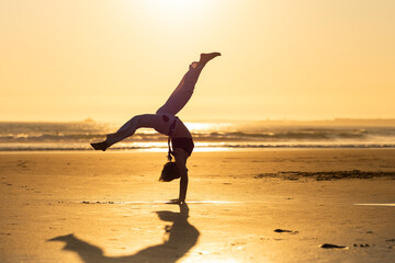 Capoeira student performing a cartwheel on beach at sunset