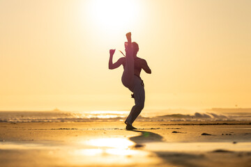 Capoeira practitioner kicking on beach at sunset