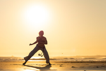 Person doing capoeira martial art on beach at sunset