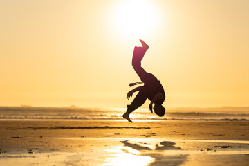 Person performing capoeira backflip on beach at sunset