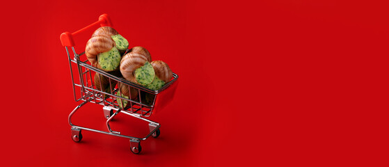 Miniature shopping cart filled with snails against a bold red background. Conceptual image with strong color contrast and ample copy space. © alesmunt