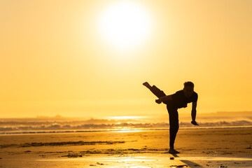 Man practicing martial art kick on beach at sunset