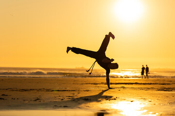 Performer balancing handstand capoeira movement on beach at sunset