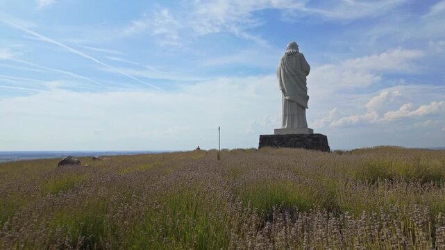 A serene push-in view of the &Aacute;ld&oacute; Krisztus statue in Tarcal, Hungary, surrounded by vibrant lavender fields and a clear autumn sky, showing cultural and spiritual heritage in a peaceful rural setting.