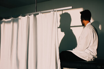 Doctor sitting in examination room with curtain and shadow silhouette
