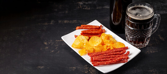 Beer and snack, chips and kabanos on a dark background.