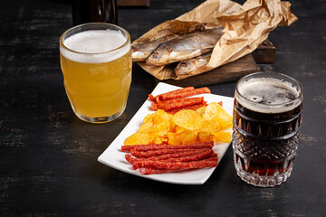 Beer and snack, chips and kabanos on a dark background.