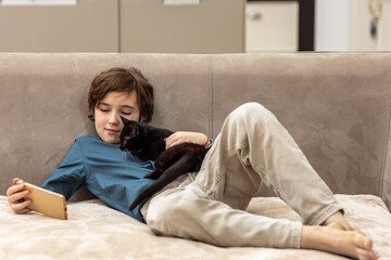 Boy playing with black kitten on sofa at home