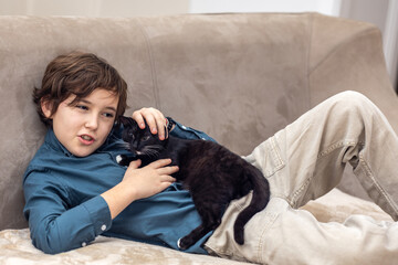 Boy playing with black kitten on sofa at home © Валентина Хруслова