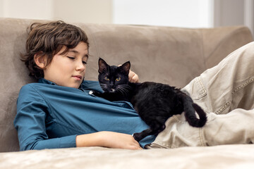 Boy playing with black kitten on sofa at home