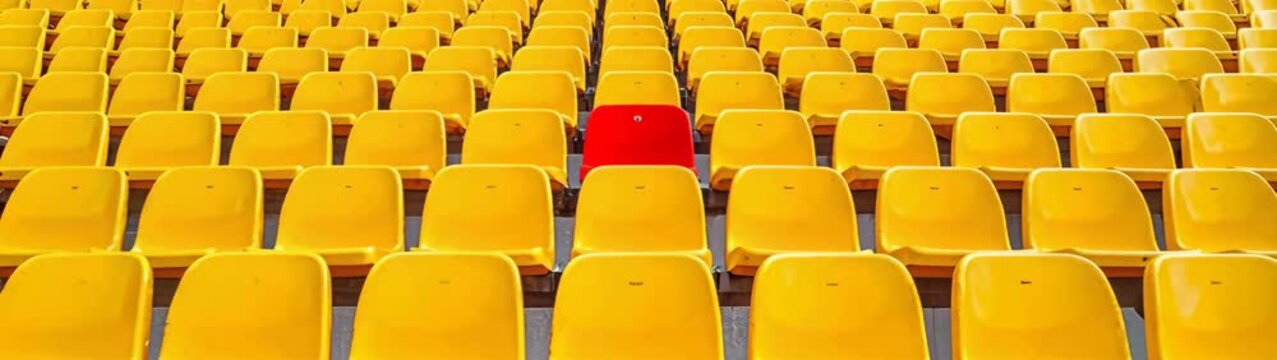 Red seat breaking pattern of empty yellow stadium seats, symbolizing individuality.