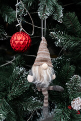 Holiday Gnome Ornament: A charming holiday gnome, adorned in a festive hat and attire, is suspended amidst the lush green boughs of a decorated evergreen tree, accompanied by a vibrant red ornament.