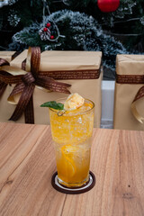Festive Citrus Delight: A vibrant orange beverage, adorned with fresh fruit, sits gracefully on a wooden surface, set against the backdrop of wrapped presents and holiday decor.