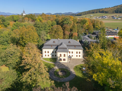 Aerial view of a cream-colored chateau nestled among vibrant autumnal trees, with a distant church spire adding to the tranquil scene, Necpaly, Zilina Region, Slovakia.