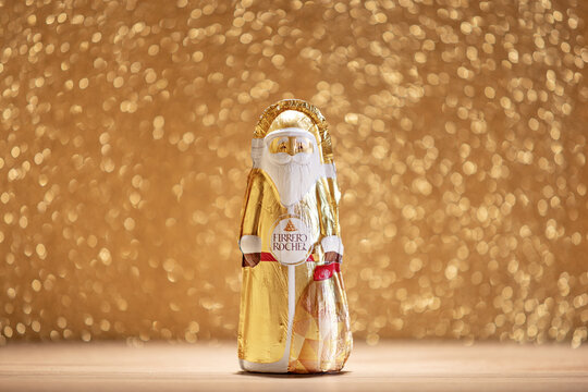 Ferrero Rocher chocolate Santa figurine wrapped in gold foil, photographed against a festive golden bokeh background. Iconic holiday confectionery product symbolizing Christmas, seasonal treats, and p