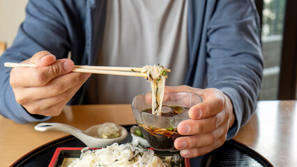 Man eating Zaru ramen (Japanese food) in a glass bowl.
