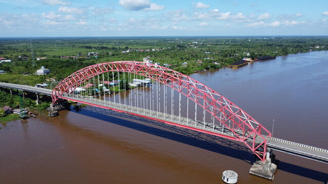 Aerial view of a tugboat pulling a barge filled with coal across the Rumpiang Bridge in the waters of South Kalimantan, Barito River
