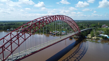 Obraz premium Aerial view of a tugboat pulling a barge filled with coal across the Rumpiang Bridge in the waters of South Kalimantan, Barito River