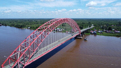 Aerial view of a tugboat pulling a barge filled with coal across the Rumpiang Bridge in the waters of South Kalimantan, Barito River