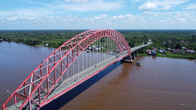 Aerial view of a tugboat pulling a barge filled with coal across the Rumpiang Bridge in the waters of South Kalimantan, Barito River