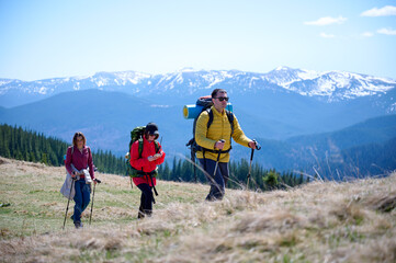 Experienced hikers walking on a mountain trail. Group of friends equipped with hiking gear climbing the mountain. Scenery of snowy mountains.