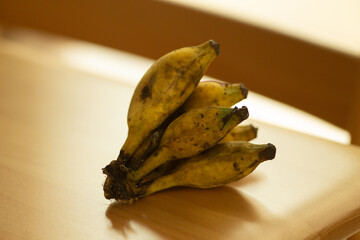 Ripe Thai Namwa bananas with natural spots placed on a wooden table, showing authentic tropical fruit texture, traditional agriculture, and everyday food from Thailand.