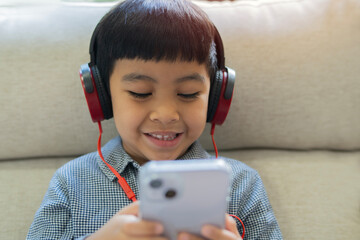 Smiling adorable schoolboy in casual shirt with headphone looking at screen of smartphone